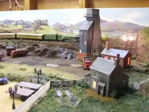 Buildings and a dump truck beside a model train track with a model train. 