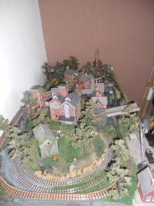 Bird's-eye perspective of model railroad with view of trees, houses, a crane, and a tower. 