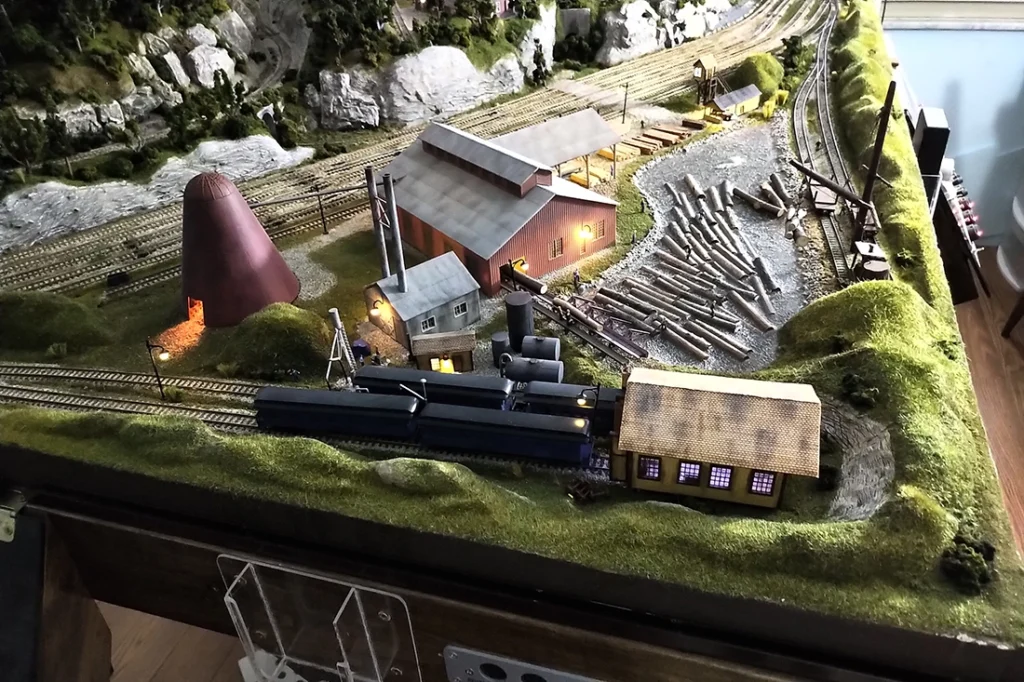 HO scale logging railroad layout featuring a detailed lumber mill scene, surrounded by realistic forest.