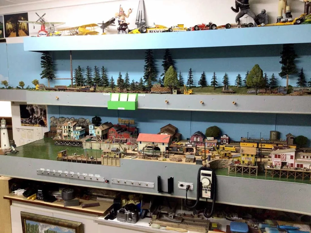 Compact HOn3 shelf layout with a narrow gauge train track, lush scenery, tiny station, bridge, and detailed miniatures.